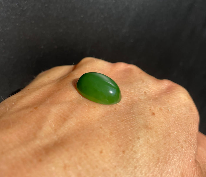 Single oval Siberian jade cabochon resting on a bare hand