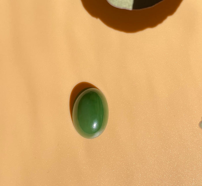 Single oval Siberian Jade cabochon on warm peach surface with soft shadow