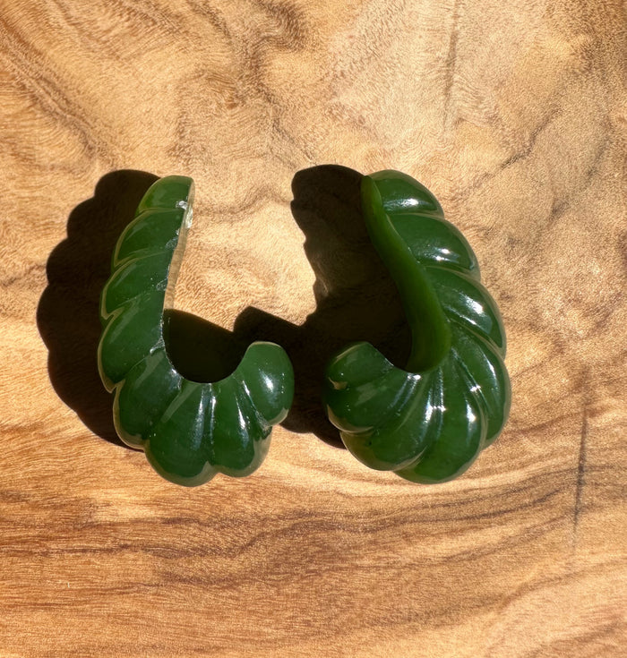 Side-angle view of two green jade fluted pieces resting on a wood tabletop