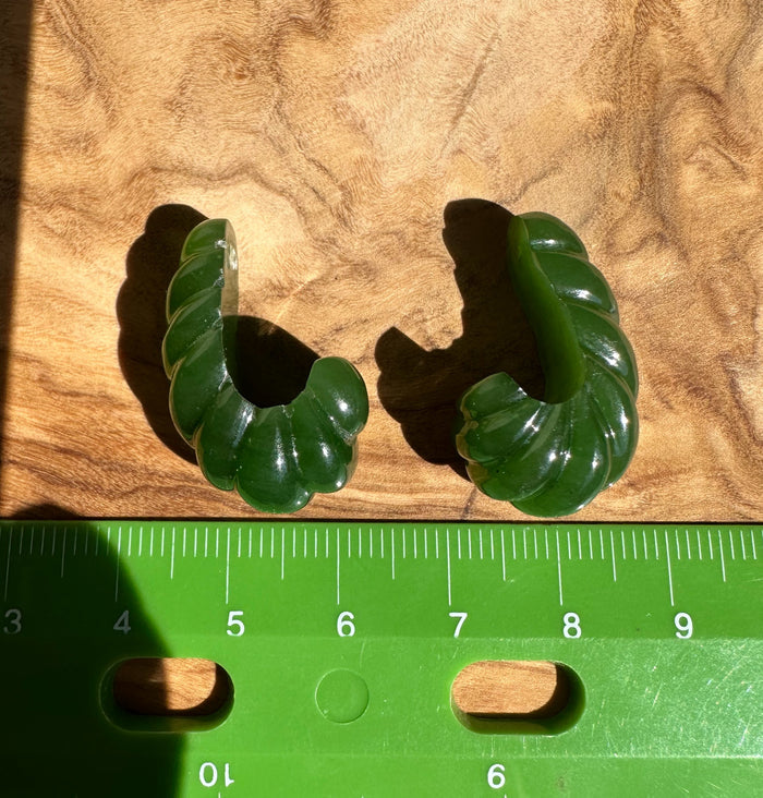 Two green jade fluted curved pieces arranged on wood with a ruler for scale
