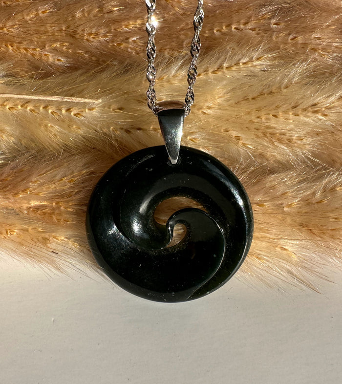 Polished black nephrite jade koru pendant with a spiral cutout on a silver chain