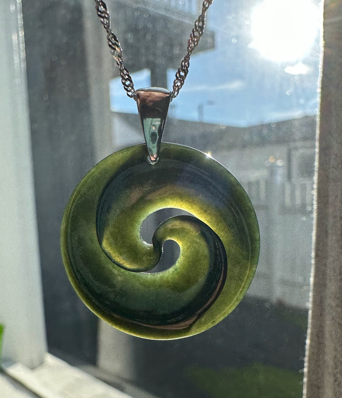 Green nephrite jade koru pendant with spiral center and silver bail on a chain.