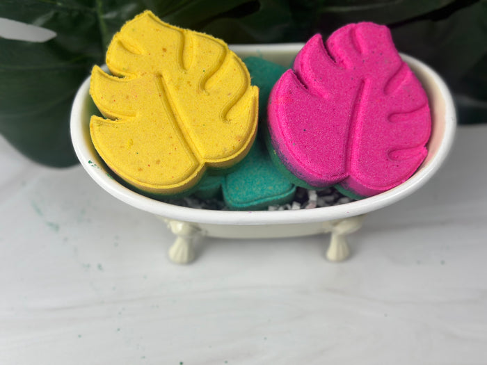 Monsterra leaf shaped yellow and pink bath bombs sitting in a white bath tub