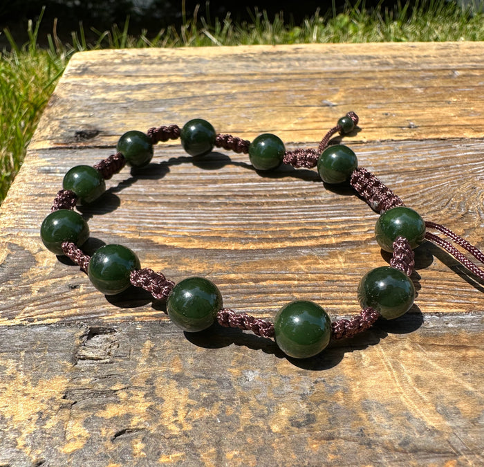 Green bead bracelet on burgundy braided cord placed on a wood surface
