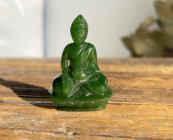 Green jade Buddha statue seated in meditation on a wooden surface.