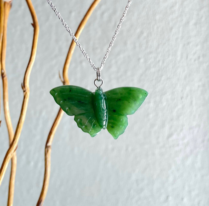 Green butterfly pendant on a silver chain hanging against a pale background.