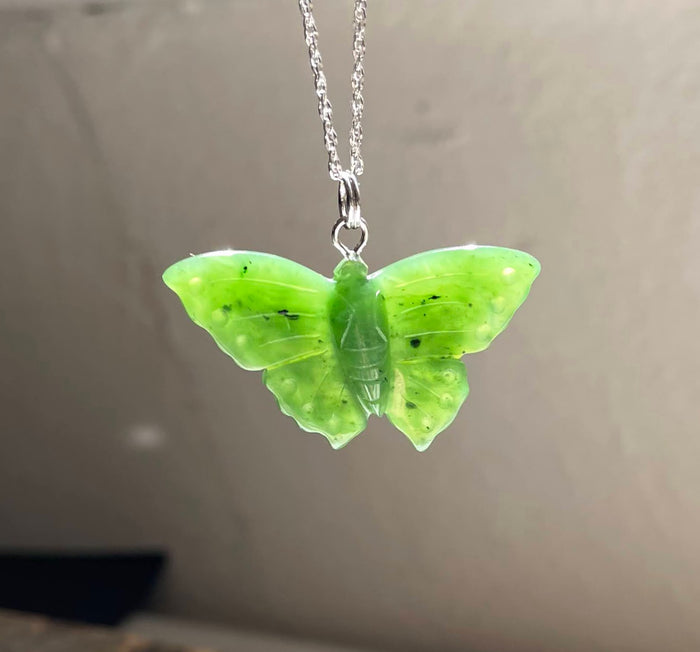 Close-up of a green butterfly pendant on a silver chain against a metallic backdrop.