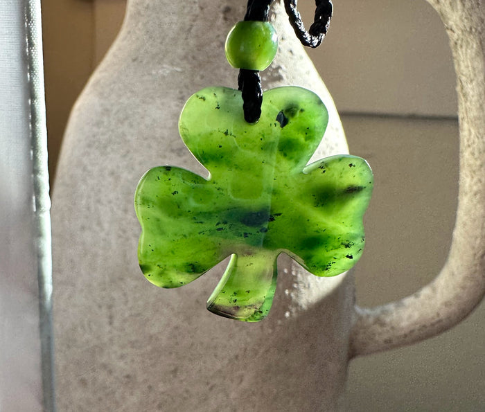 Close-up of a green jade three leaf clover pendant on a black cord
