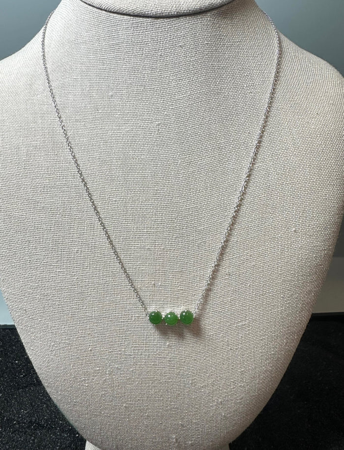 Three green jade beads on a silver chain necklace displayed on a mannequin bust.