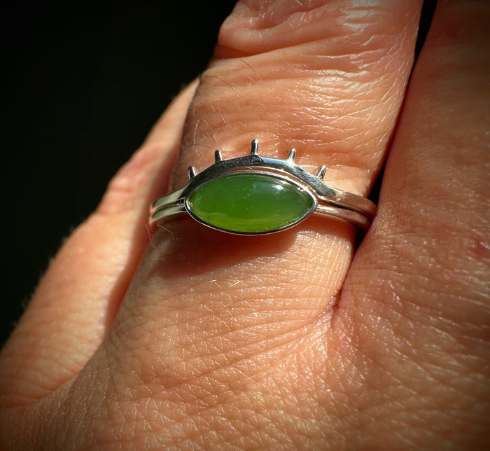 Two slim silver bands frame a bright green oval jade on a finger