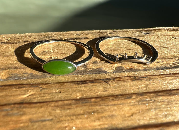 Two silver eye rings with green jade stones laid on a rustic wooden surface