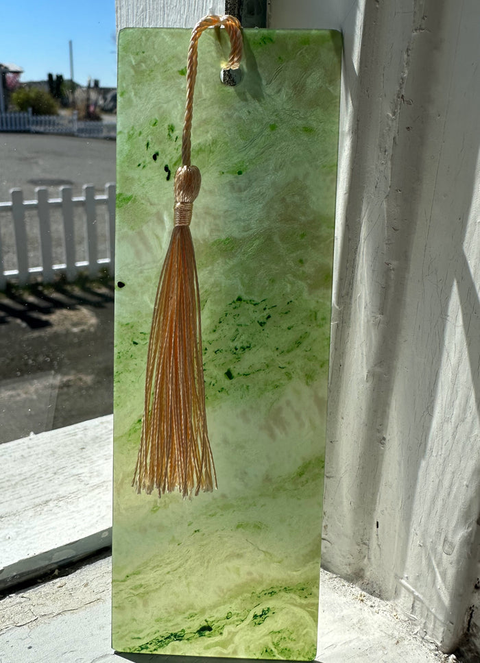 Green jade bookmark six inches long with a tan tassel hanging from a top hole marbled light and dark green pattern