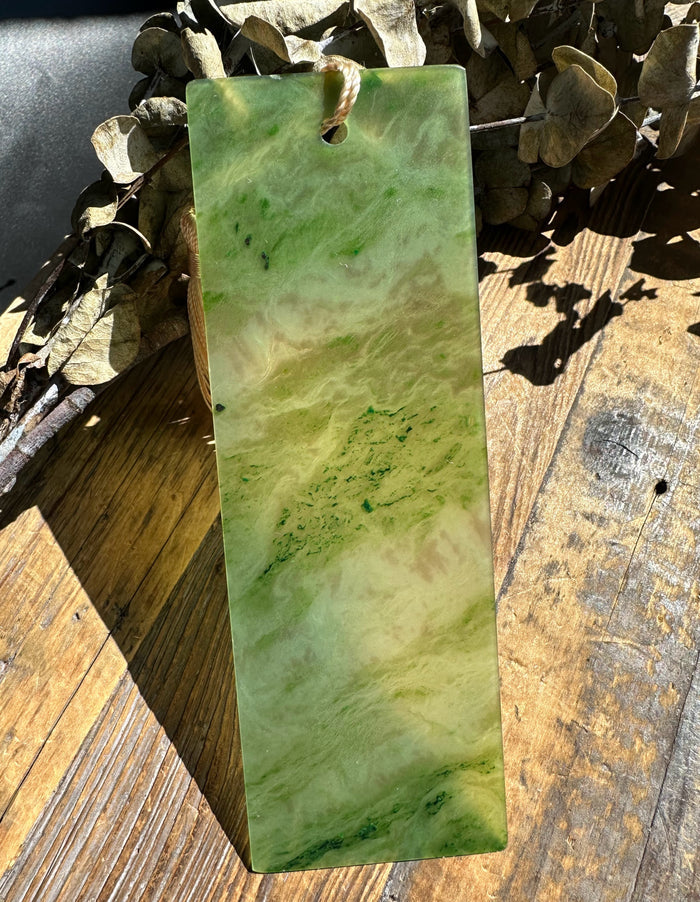 Rectangular green jade bookmark six inches long with marbled pattern resting on a wooden surface with dried leaves nearby