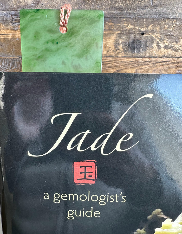 Green jade bookmark resting on a glossy black book cover that reads Jade a gemologist's guide.