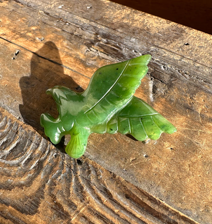 Green jade eagle brooch with carved wings resting on a weathered wooden surface