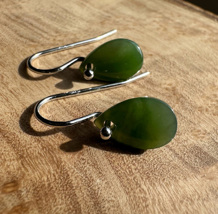 Pair of green jade teardrop earrings with silver hooks on a wooden surface