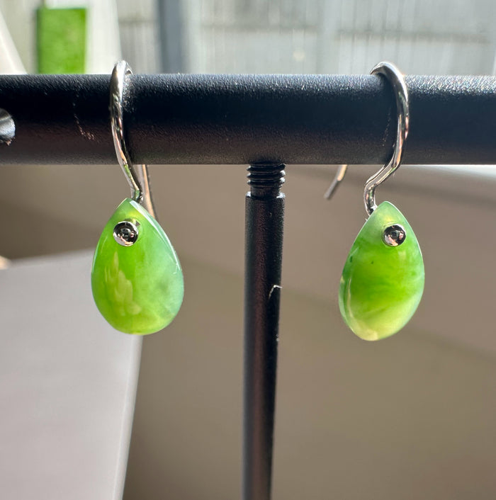 Close-up of green jade teardrop earrings with silver hooks on a display stand