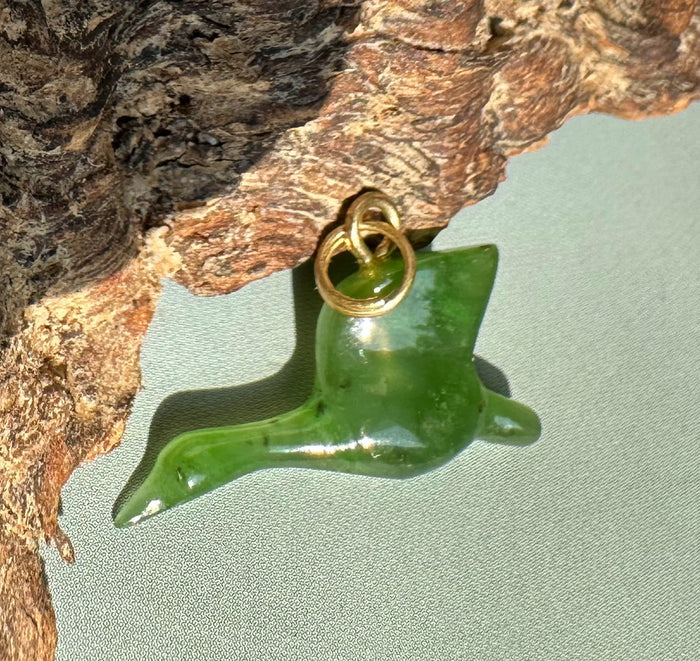Green jade goose charm with a gold ring bail attached to rough tree bark background