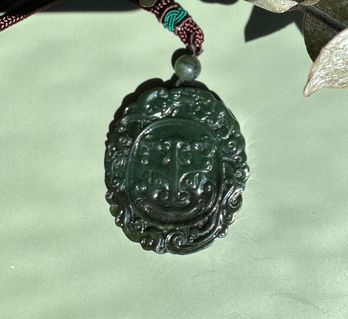 Round carved green jade pendant on a brown braided cord with a small bead above