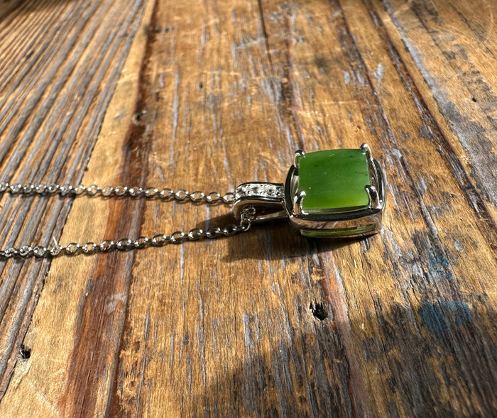 Canadian Jade Pendant with CZ featuring a square green jade stone in a silver setting on a chain against a wooden surface.