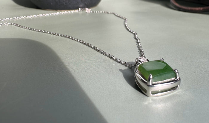 Canadian Jade Pendant with CZ on a silver chain with a diamond-studded bail resting on a pale backdrop.