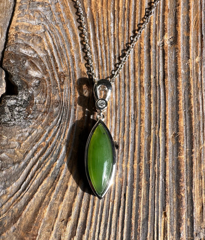Canadian Jade pendant with CZ a vivid green marquise jade stone set in silver bezel on a silver chain against wood