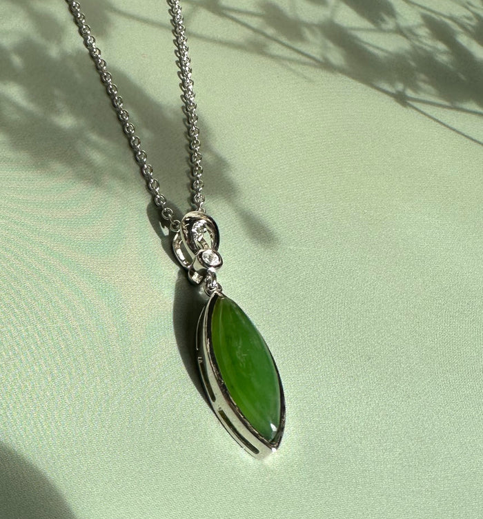 Green jade pendant with CZ set in a silver bezel on a silver chain against pale green fabric