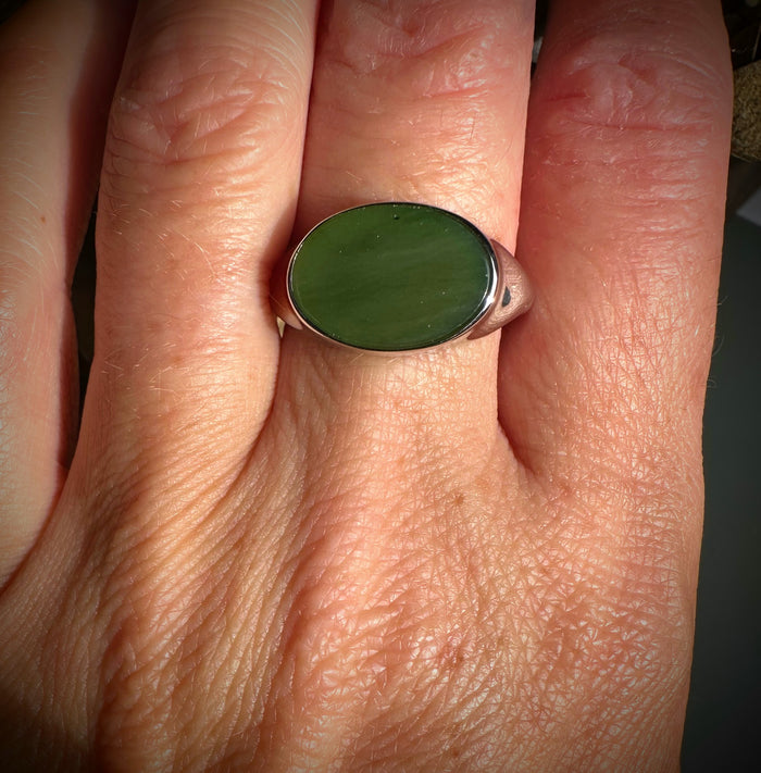 Green oval jade ring set in a silver band worn on a finger