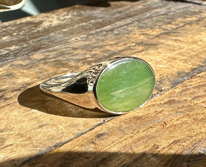 Green jade ring with oval cabochon displayed on a sunlit wooden surface
