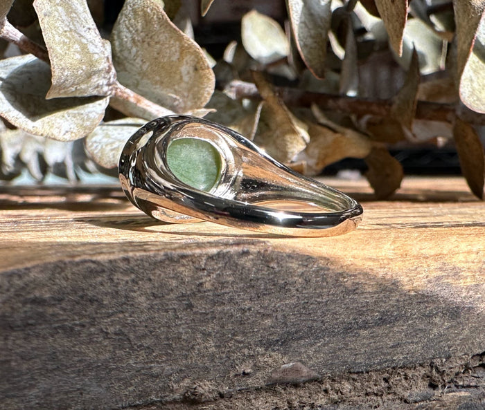 Side view of green jade ring on wood with polished silver bezel and shank