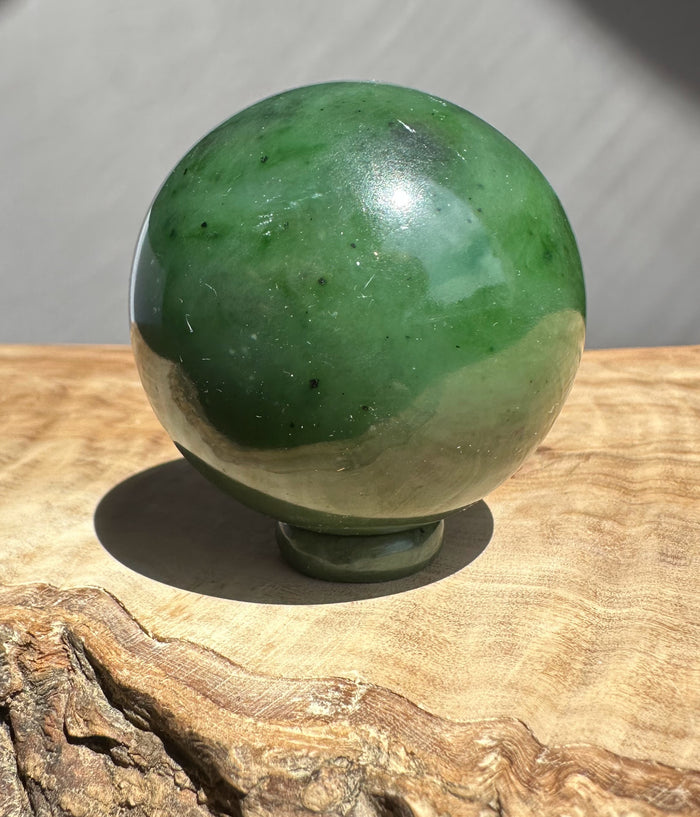 Green jade sphere on a wooden surface with a neutral background