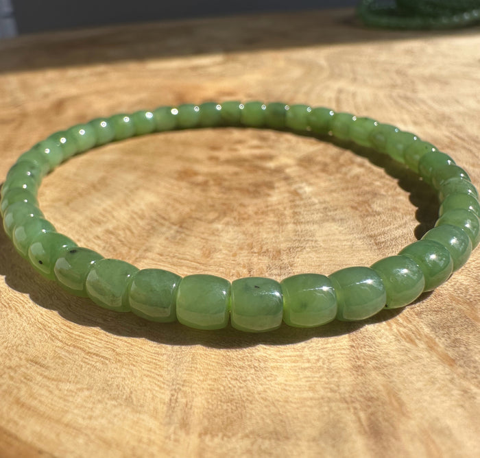 Close up of Canadian nephrite jade bead bracelet with glossy green beads on a wooden surface.