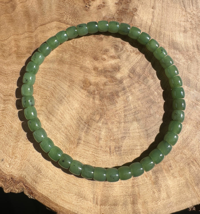 Canadian nephrite jade bead bracelet with rounded green beads and small dark inclusions on a wooden surface.