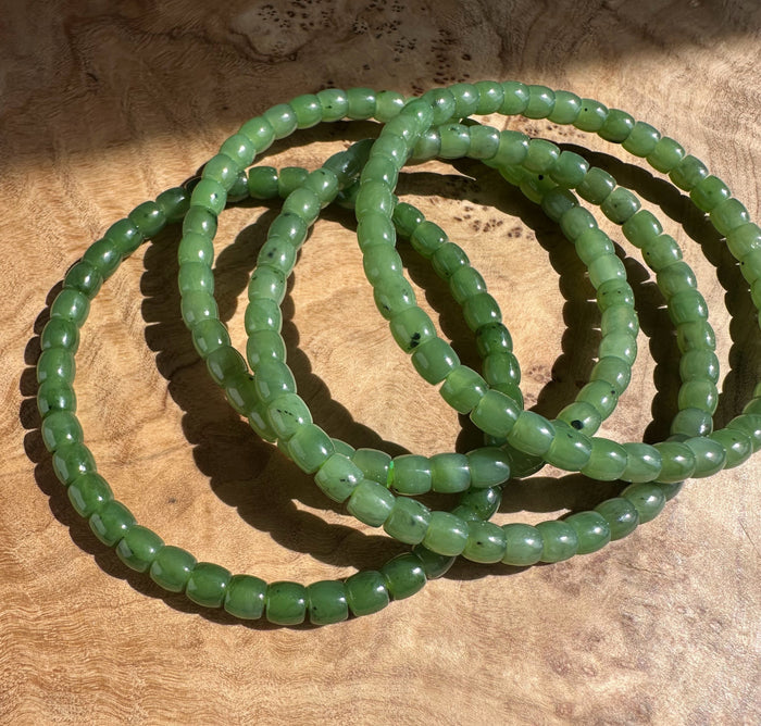 Close-up of pale green nephrite jade beads forming the Canadian Nephrite Jade Bead Bracelet King Mountain Mine on a wood surface.