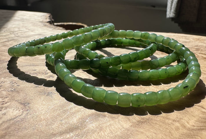 Canadian Nephrite Jade Bead Bracelet King Mountain Mine coiled on sunlit wood.