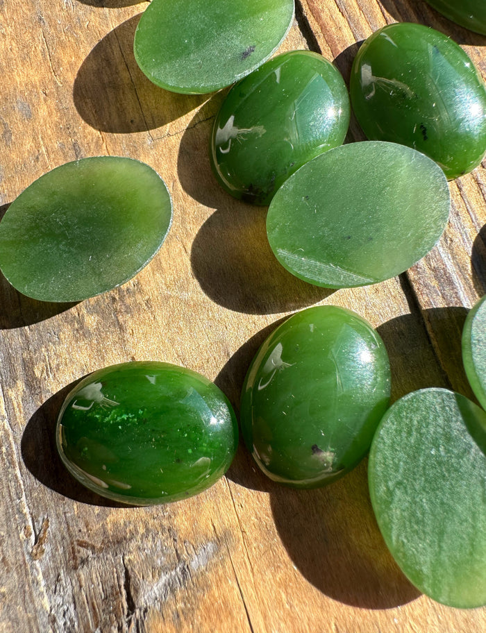 Green nephrite jade oval cabochons 15 by 20 mm sold individually with smooth domed fronts on a wood background