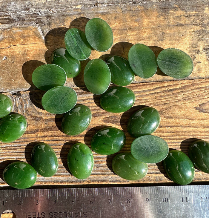 Green nephrite jade oval cabochons scattered on wood with a ruler for scale
