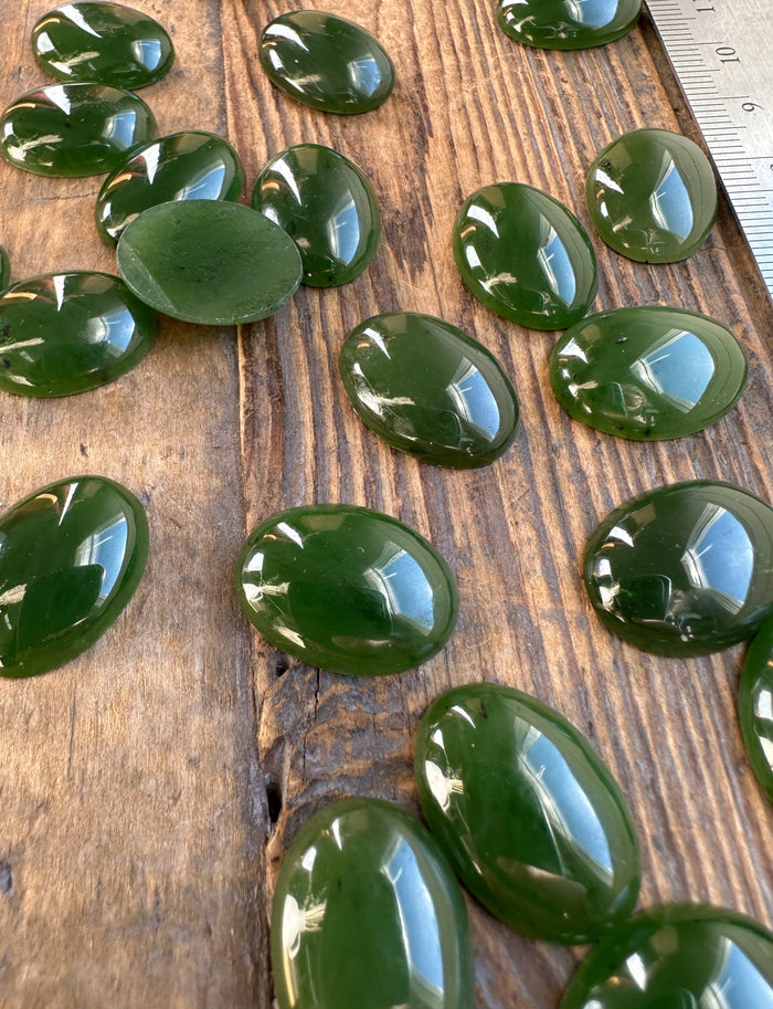 Group of polished Canadian nephrite jade oval cabochons on a rustic wood surface with a ruler for scale