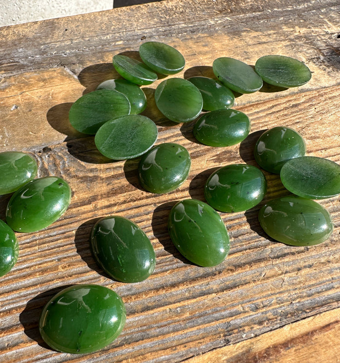 Canadian nephrite jade oval cabochons scattered on wooden tabletop with visible grain and reflections