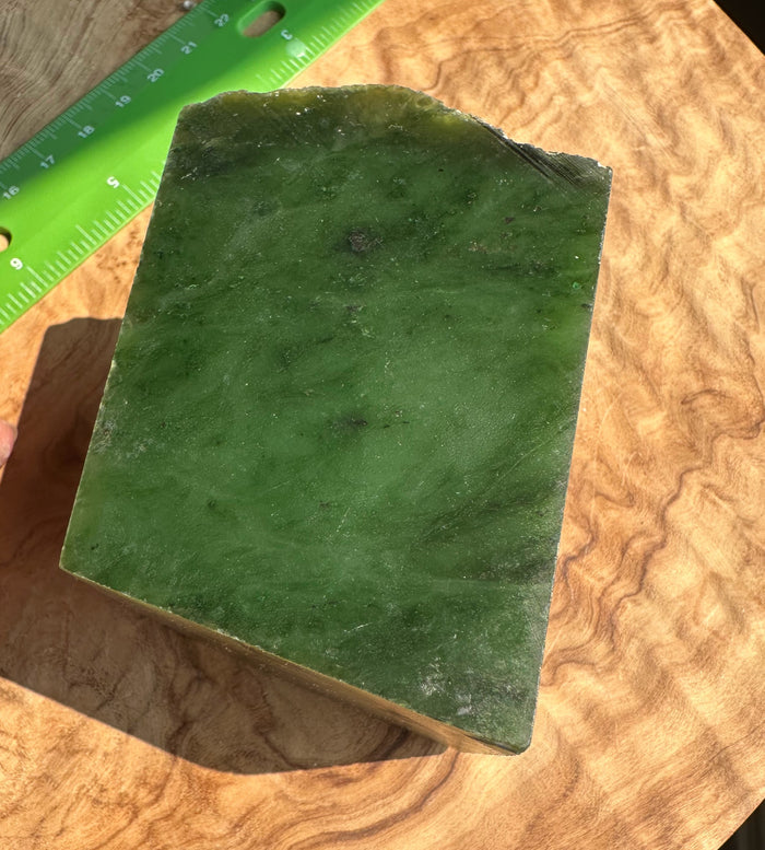A rectangular green jade with natural marbling, photographed on a wood-grain surface with a green ruler partially visible at the top left for scale.