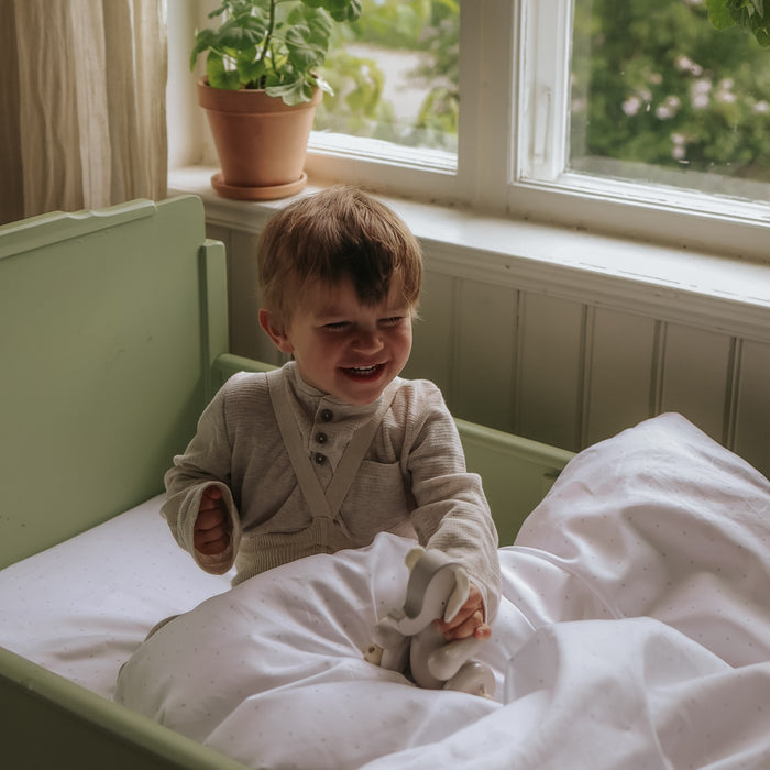 Child sitting in a crib laughing with a plant on a windowsill in the background