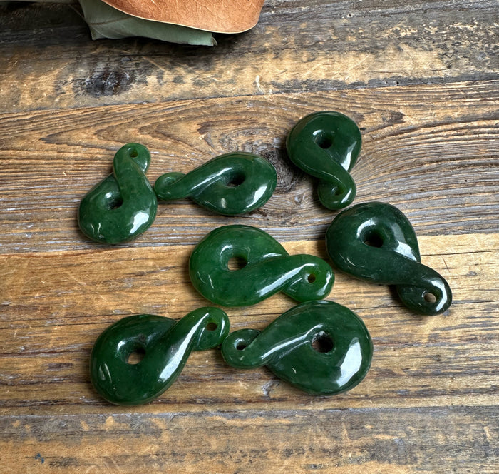 Dark green jade infinity twist pendants with holes arranged on a rustic wooden surface