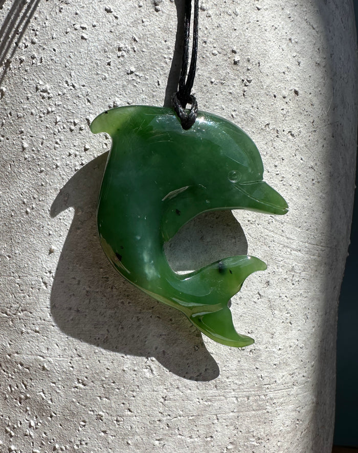 Dolphin-shaped green jade pendant hanging on a black cord