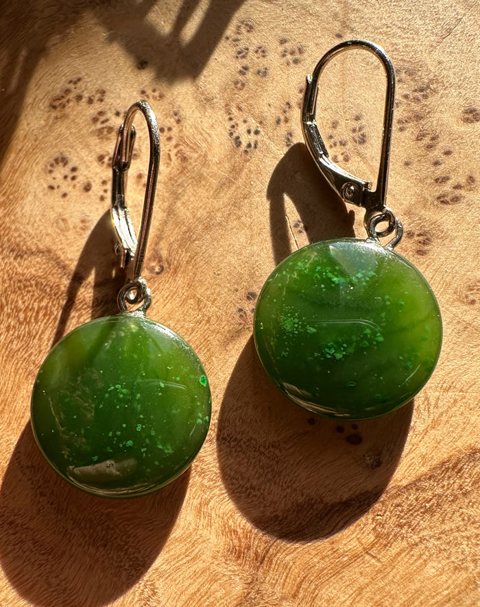 Pair of green round stone earrings with leverback silver hooks on a wooden surface
