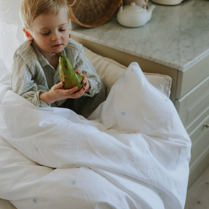 Child holding a green pear in a cozy indoor setting under a toddler duvet embroidered with blue stars.