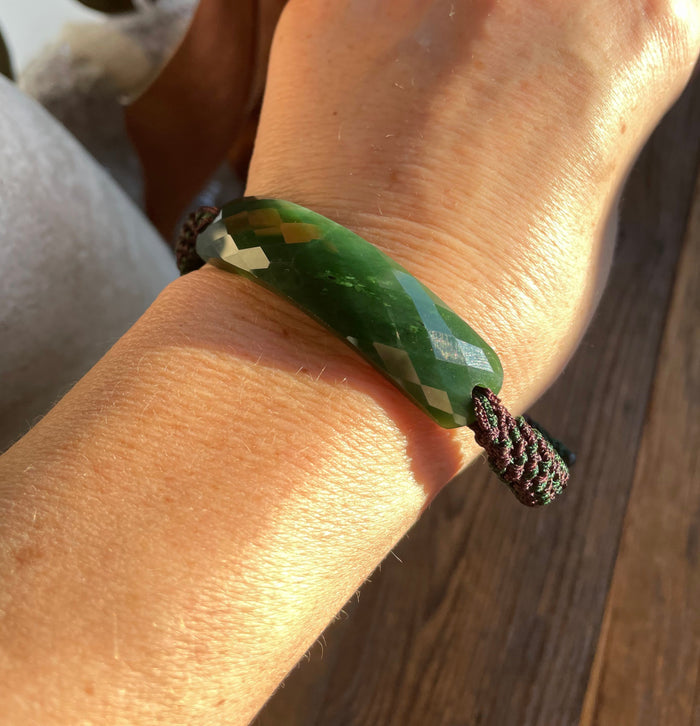 Green jade faceted bracelet on a wrist tied with a burgundy braided cord.