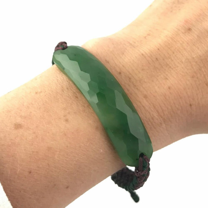 Close up of green jade faceted bracelet on the wrist against a light background.