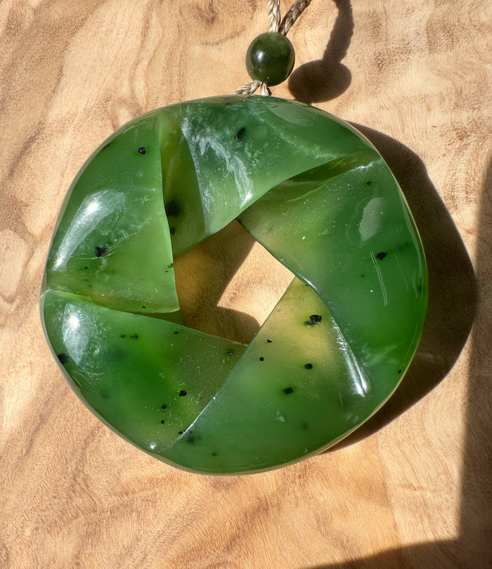 Green nephrite jade circular pendant with four curved segments forming a hollow center on a beige rope with a green bead.