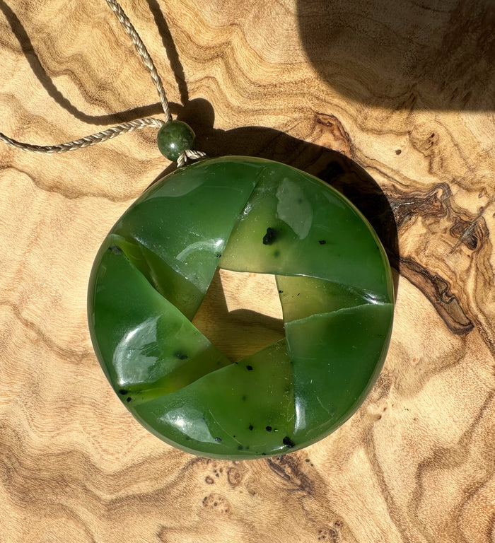 Circular fractured nephrite jade pendant in green tones on a braided cord with a small green bead