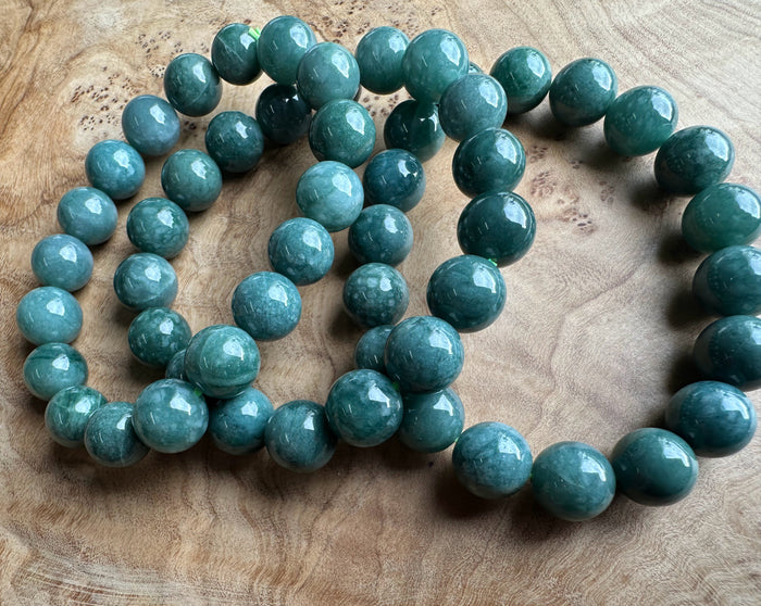 Teal-green jadeite beads 10mm laid on a wooden surface, glossy round stones